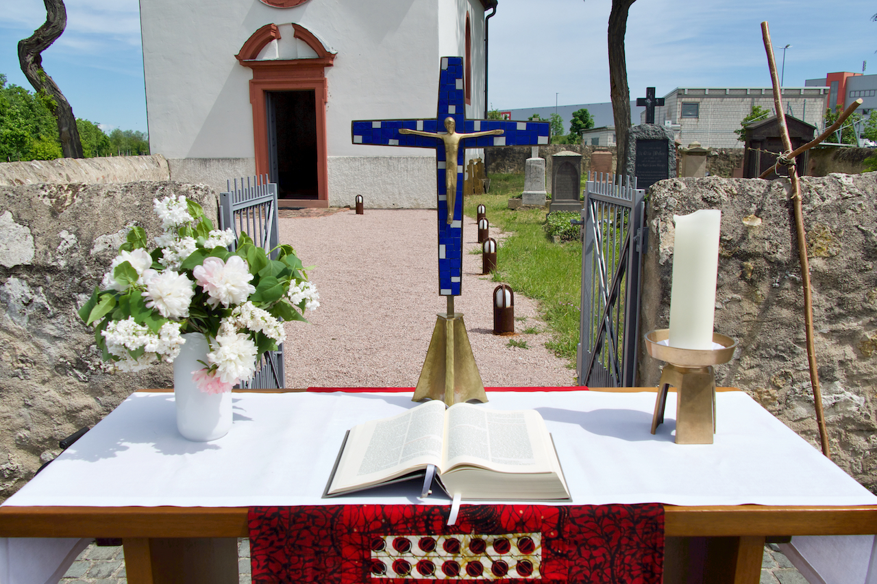Der Altar mit weißen Blumen, einem blauen Kreuz, einer Kerze und der aufgeschlagenen Bibel vor der Mönchhofkapelle